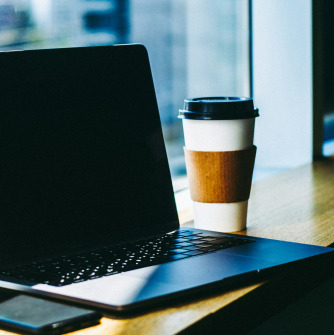 Image of a laptop on a table with a cup of coffee