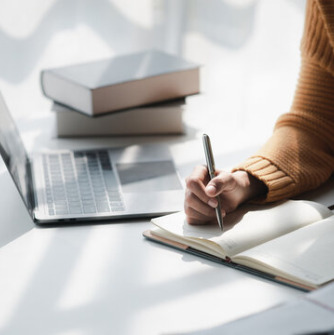 Laptop, textbooks, and student writing in notebook