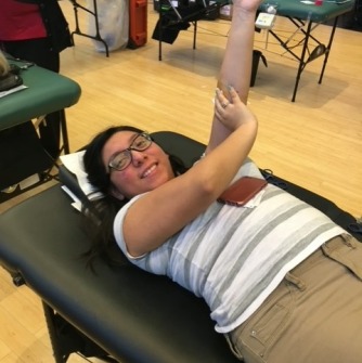 Student lying on a stretcher and raising their arm as they finish donating blood