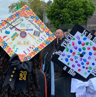 Two students from behind showing off their decorated graduation caps outside after commencement