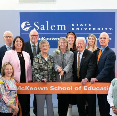 Individuals standing behind an orange ribbon taking part in a ribbon cutting ceremony for the McKeown School of Education