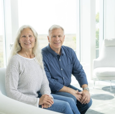 Kim Gassett-Schiller seated on a couch alongside her husband, Philip Schiller