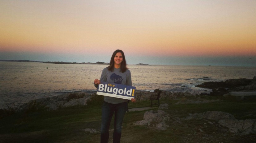 A student holds a University of Wisconsin banner while standing at the beach at sunset. 