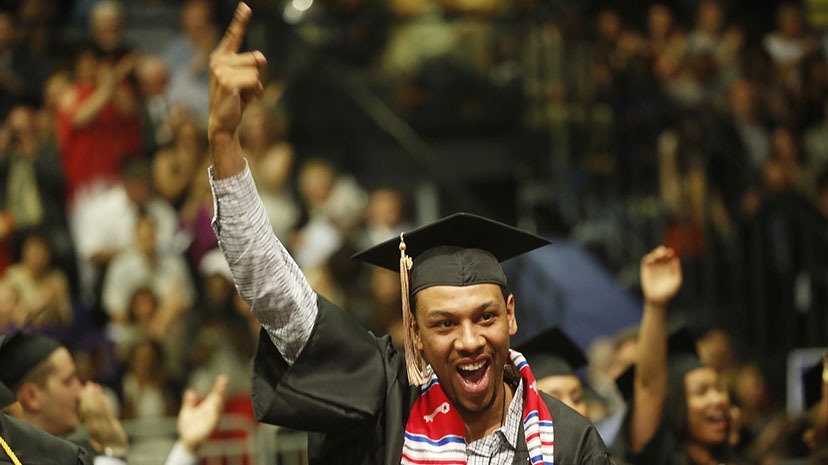 A student celebrates at commencement by pointing "I'm number 1"