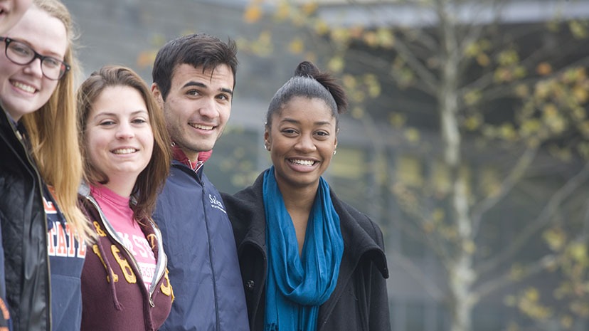 A group of students of diverse backgrounds enjoy a fall day on campus