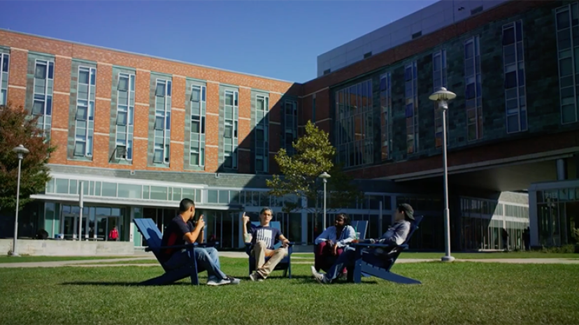 Four students sitting in Adirondack chairs on the March quad